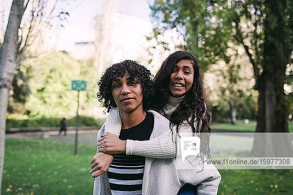 Junge mit lockigem Haar nimmt lächelnde Schwester im Park huckepack