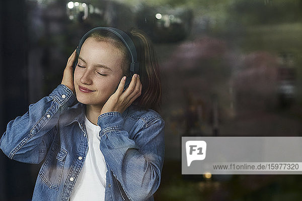 Vorpubertäres Mädchen mit geschlossenen Augen  das zu Hause über Kopfhörer Musik hört