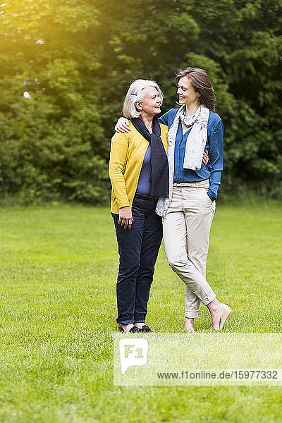 Glückliche ältere Frau und erwachsene Tochter stehen auf einer Wiese in einem Park und schauen sich an