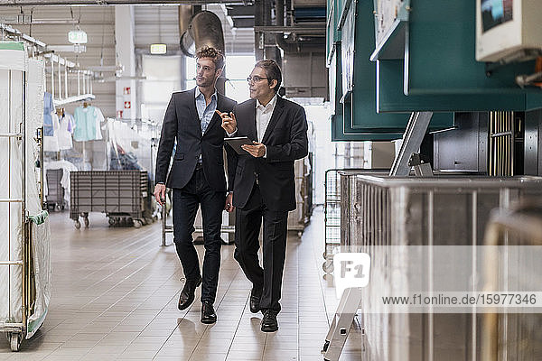 Zwei Geschäftsleute mit Tablette zu Fuß in einer Fabrik