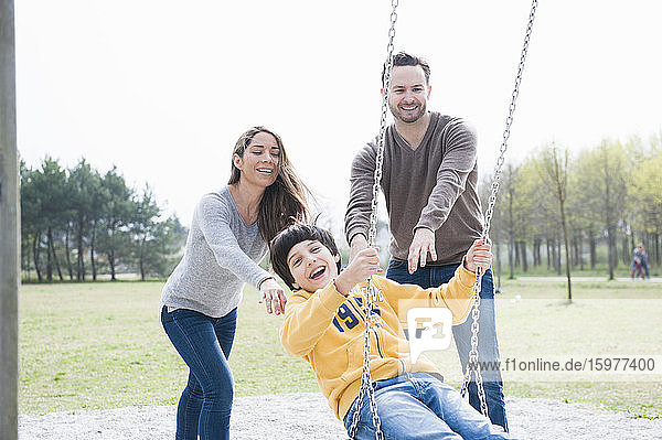 Glückliche Eltern  die ihren Sohn auf einer Schaukel im Park gegen den klaren Himmel schieben
