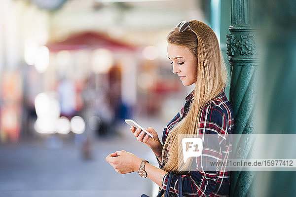 Junge Frau lehnt an einer Säule und schaut auf ihr Smartphone