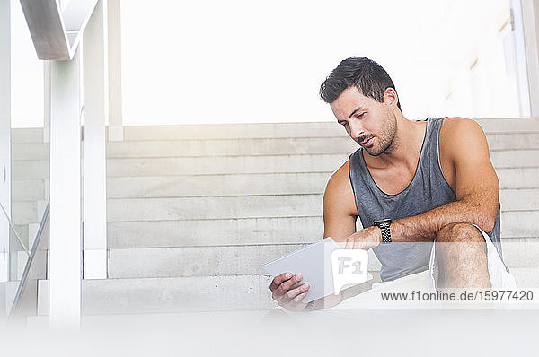 Porträt eines jungen Mannes  der auf einer Treppe sitzt und ein Tablet benutzt