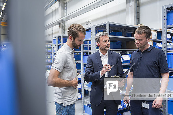 Three men talking in storehouse of a factory