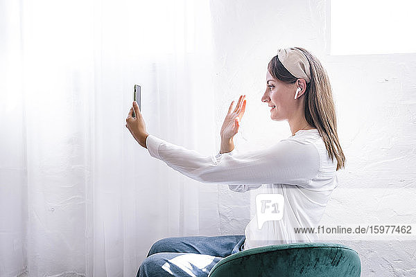 Smiling woman waving while enjoying video call through smart phone at home