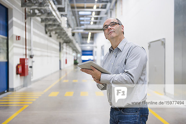 Geschäftsmann hält Tablette auf dem Korridor in einer Fabrik