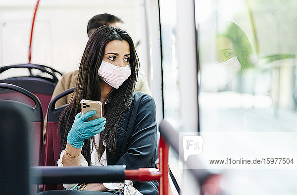 Porträt einer jungen Frau mit Schutzmaske im Bus  die aus dem Fenster schaut  Spanien