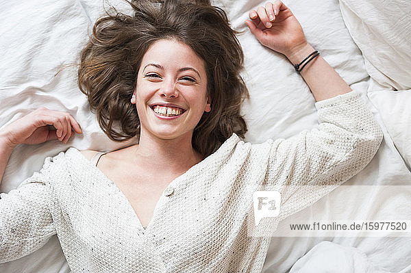 Cheerful young woman lying in bed at home