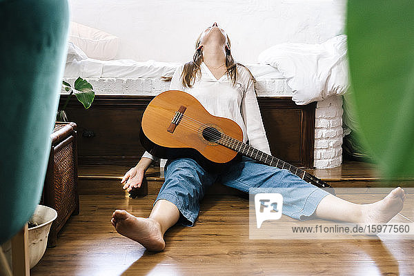 Frau mit Gitarre auf dem Boden vor dem Bett sitzend