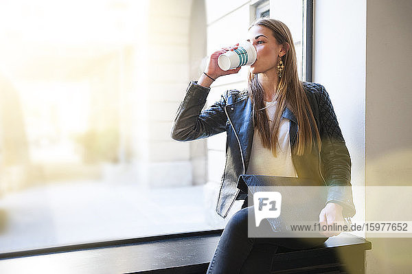 Junge Frau trinkt Kaffee und hält einen Laptop auf der Fensterbank eines Cafés