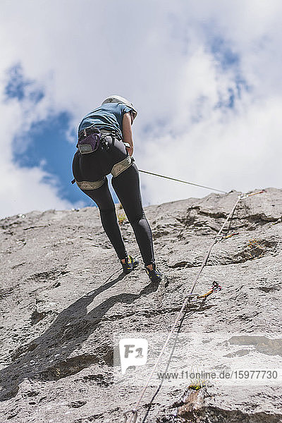 Young woman rappelling down while rock climbing against sky on sunny day