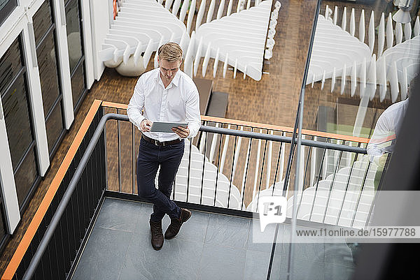 Geschäftsmann steht auf der Galerie eines modernen Büros und benutzt ein Digitaltablett