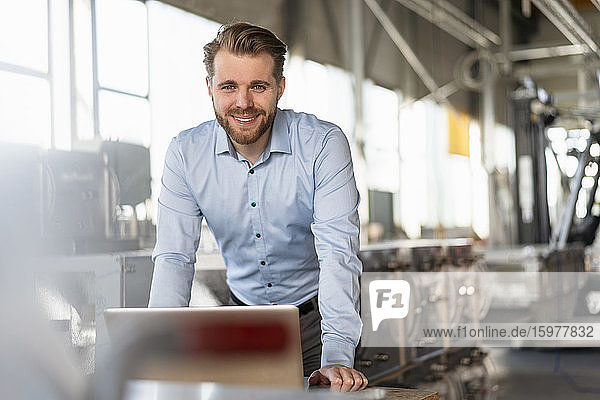 Portrait of smiling young businessman with laptop in a factory