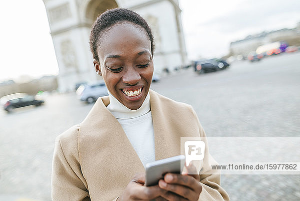 Glückliche junge Frau mit Smartphone vor dem Arc de Triomphe an einem sonnigen Tag  Paris  Frankreich