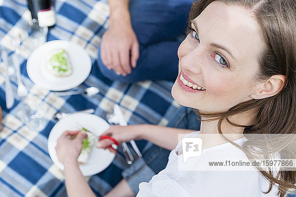 Porträt einer lächelnden schönen Frau  die mit einem Mann zusammensitzt und ein Picknick genießt