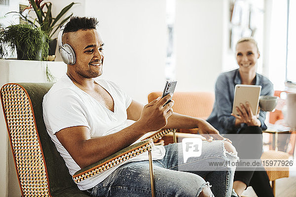 Smiling man sitting in armchair listening music with headphones and smartphone