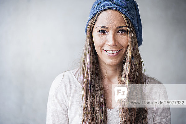 Happy woman with long brown hair wearing knit hat against gray wall