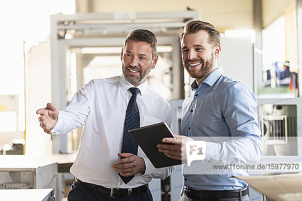 Zwei lächelnde Geschäftsleute mit Tablette haben eine Sitzung in einer Fabrik