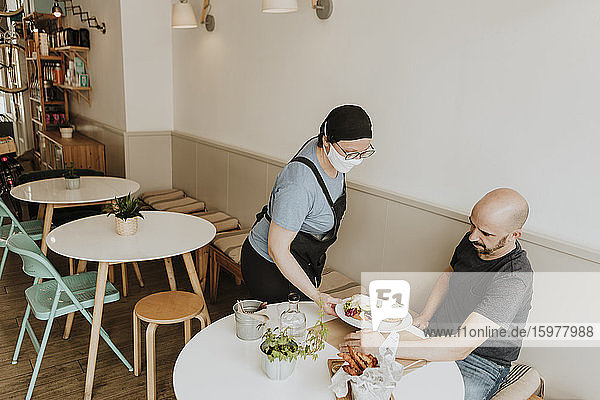 Kellnerin mit Schutzmaske serviert Essen in einem Café