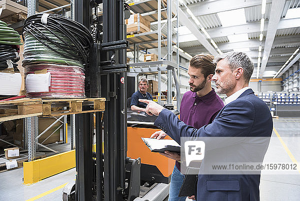 Two men and worker on forklift in high rack warehouse