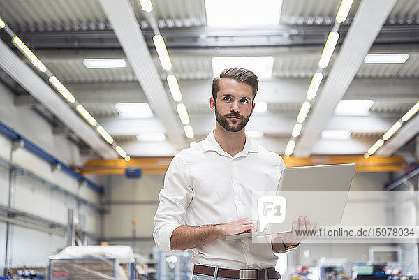Young man holding laptop on factory shop floor