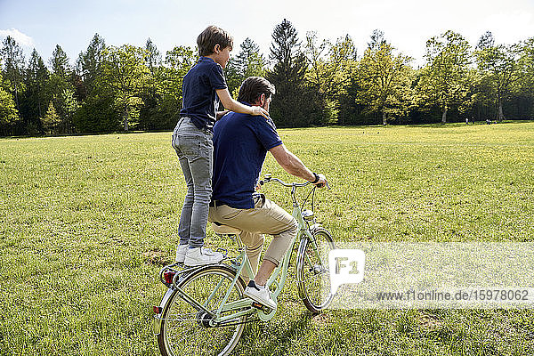 Vater und Sohn genießen eine Fahrradtour im Gras an einem sonnigen Tag