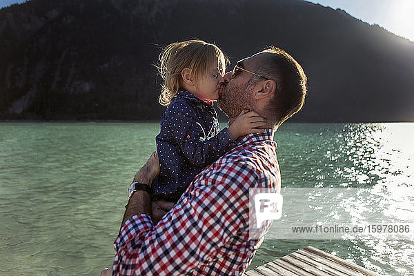 Vater und Tochter küssen sich vor einem Berg und einem See am Achensee  Bundesland Tirol  Österreich
