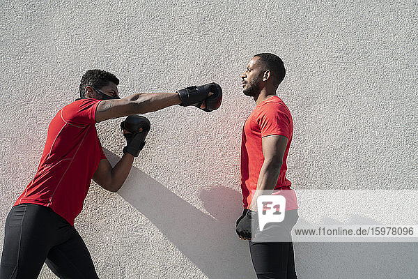 Sportsman wearing face mask and boxing against training partner standing still