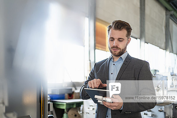 Young businessman with tablet and workpiece in a factory