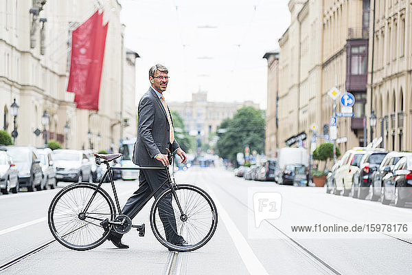 Businessman wearing suit with bicycle crossing road in city
