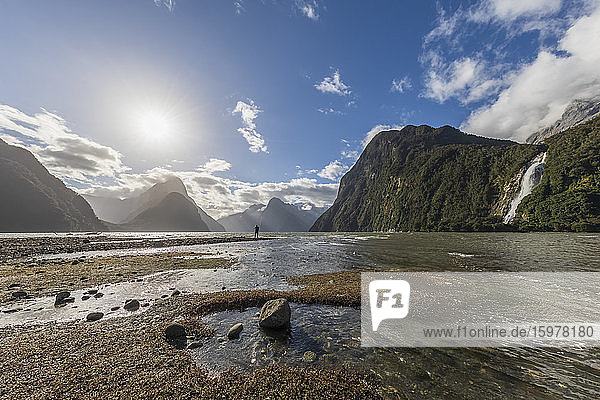 New Zealand  Sun shining over Milford Sound beach during low tide with Bowen Falls in background
