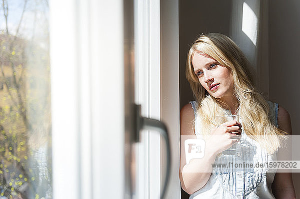 Porträt einer ernsten blonden Frau  die aus dem Fenster schaut