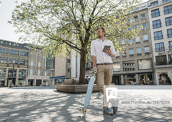 Businessman with tablet and skateboard in the city