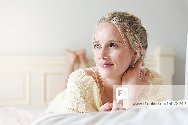 Porträt einer lächelnden blonden Frau mit blauen Augen auf dem Bett liegend