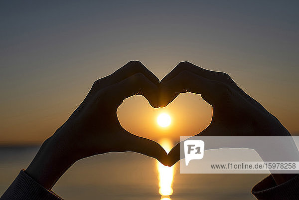 Germany  Mecklenburg-West Pomerania  Poel Island  Silhouette of hands making heart shape by sea at sunset