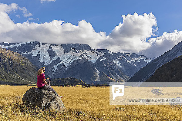 New Zealand  Oceania  South Island  Canterbury  Ben Ohau  Southern Alps (New Zealand Alps)  Mount Cook National Park  Aoraki / Mount Cook  Woman sitting on boulder in mountain landscape