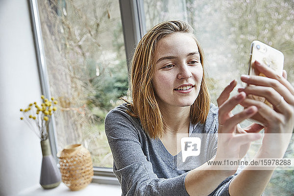 Porträt einer jungen Frau  die zu Hause ein Selfie mit ihrem Smartphone macht