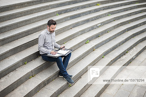 Geschäftsmann in voller Länge  der ein Dokument analysiert  während er auf den Stufen des Amphitheaters sitzt