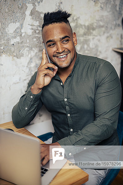 Porträt eines lächelnden jungen Mannes am Telefon bei der Arbeit im Home Office