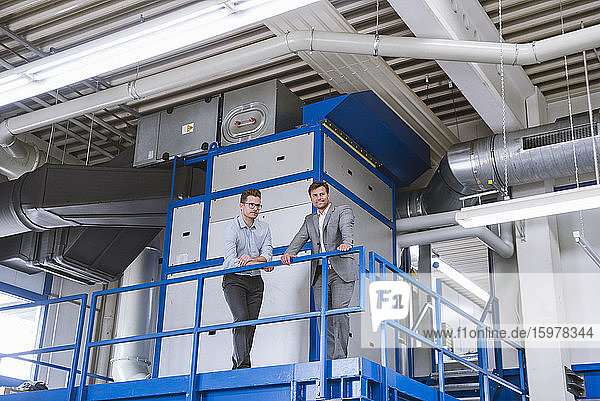 Zwei Geschäftsleute stehen im oberen Stockwerk einer Fabrik