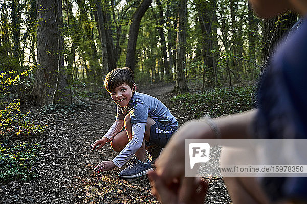 Lächelnder Junge hockt vor seiner Schwester im Wald