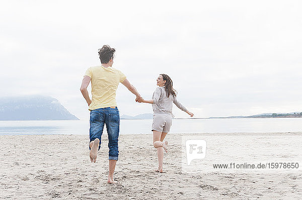 Happy couple running hand in hand on the beach  Sardinia  Italy