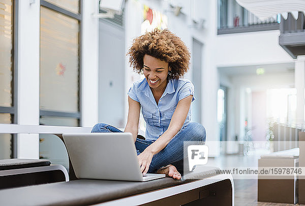 Junge Frau sitzt auf einer Bank in einem modernen Büro und benutzt einen Laptop