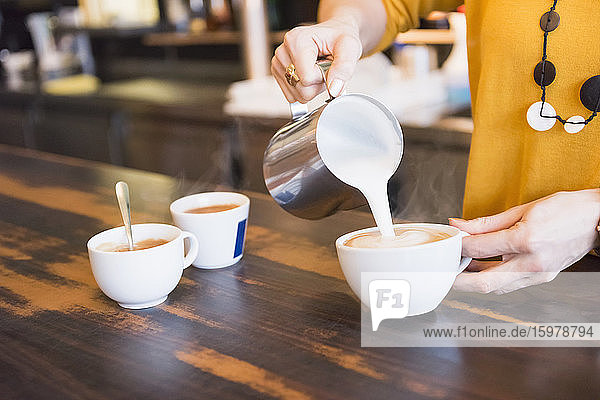 Weiblicher Barista bereitet Cappuccino an einem Holztisch in einem Café zu