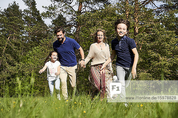 Lächelnde Familie läuft auf Gras gegen Bäume an einem sonnigen Tag