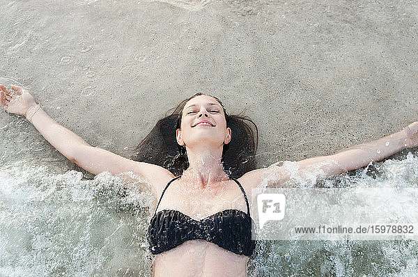 Porträt einer glücklichen Frau im Bikini  die am Meeresufer liegt und die Brandung genießt  Sardinien  Italien