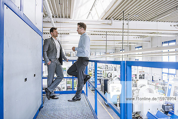 Zwei Geschäftsleute unterhalten sich im oberen Stockwerk einer Fabrik