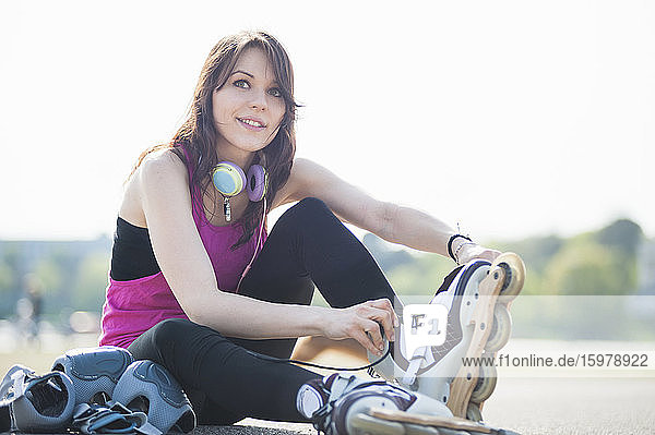 Lächelnde  zuversichtliche junge Frau  die Inline-Skates trägt  während sie gegen den klaren Himmel im Park sitzt
