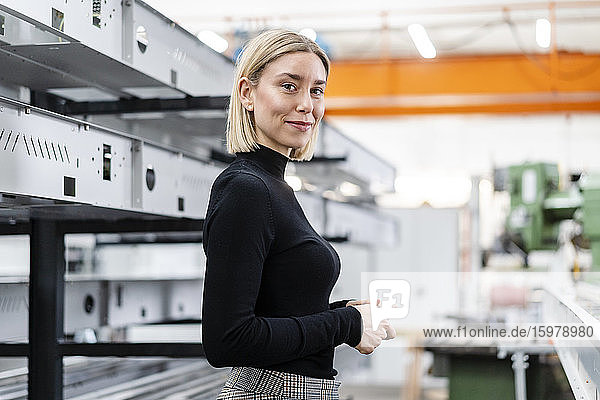 Porträt einer lächelnden Frau an Metallstäben in einer Fabrikhalle