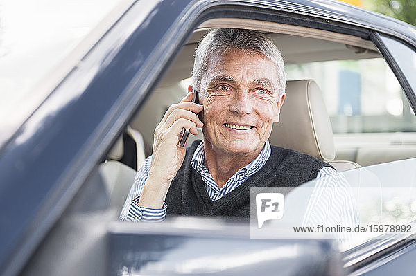 Porträt eines lächelnden älteren Geschäftsmannes beim Telefonieren im Auto